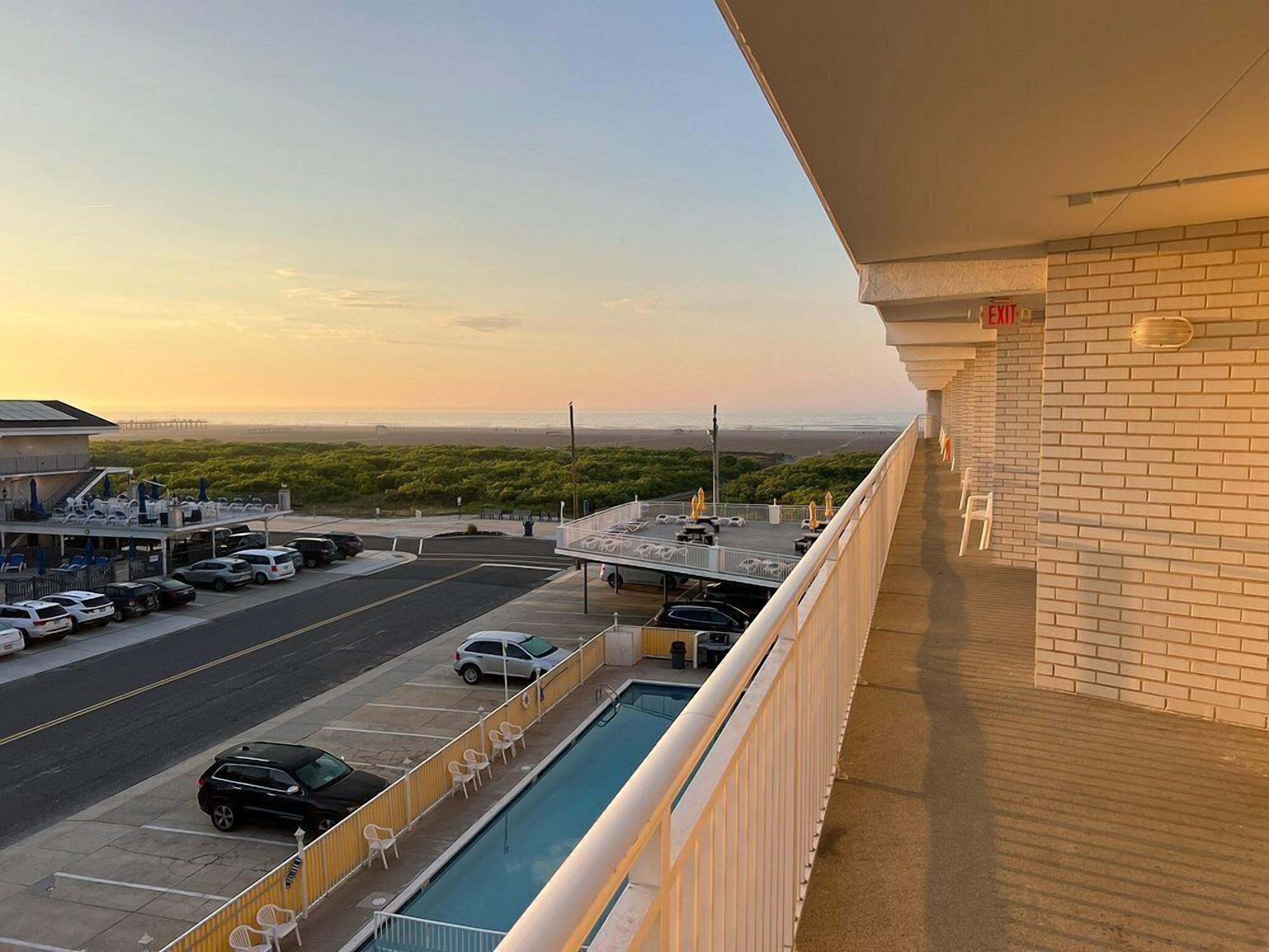 A hotel balcony with a view of a parking lot and a beach.