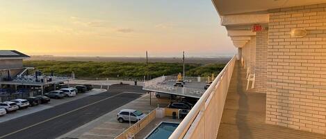 A hotel balcony with a view of a parking lot and a beach.