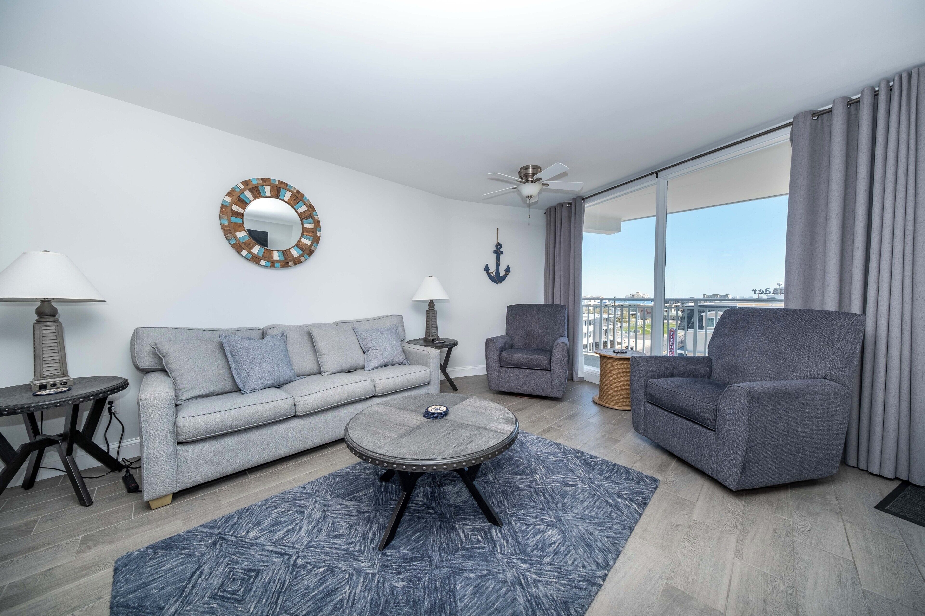 Una sala de estar moderna con un sofá, un sillón, una mesa de centro redonda y vistas a la ciudad a través de amplias ventanas.