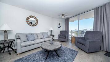 Una sala de estar moderna con un sofá, un sillón, una mesa de centro redonda y vistas a la ciudad a través de amplias ventanas.