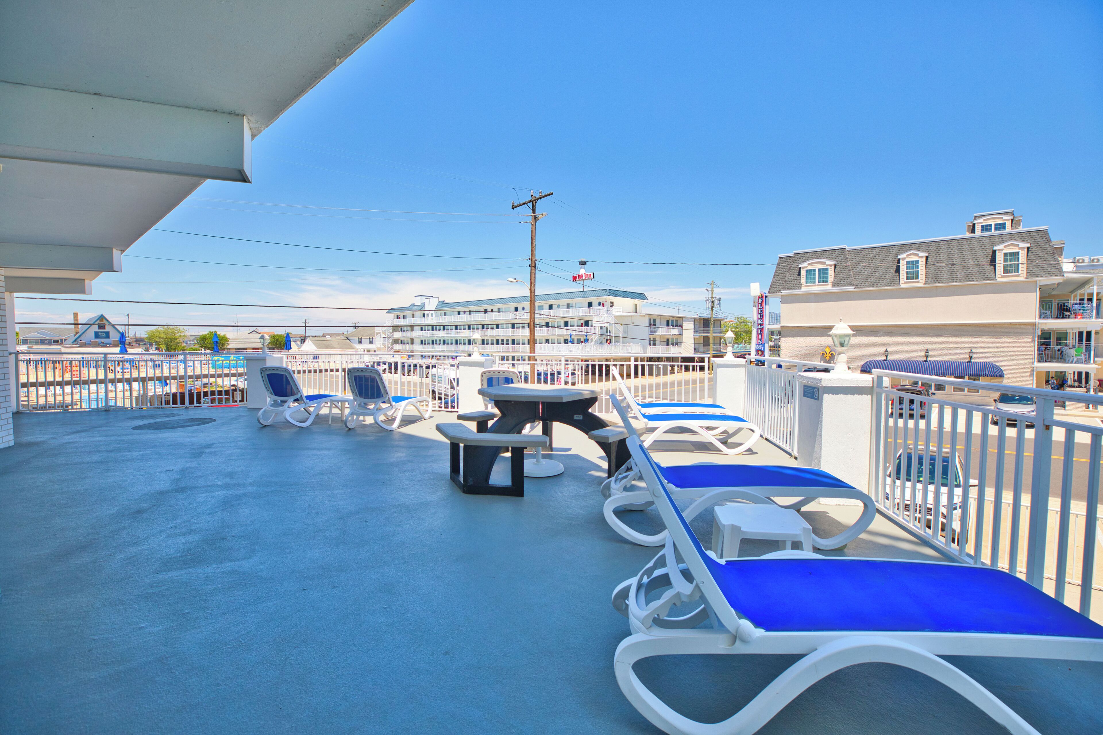 A rooftop deck with lounge chairs, a picnic table, and a view of a hotel building.