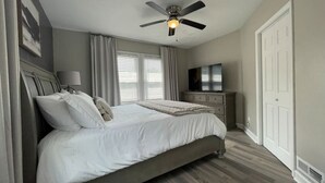 A bedroom with a bed, a ceiling fan, a TV, and a dresser.
