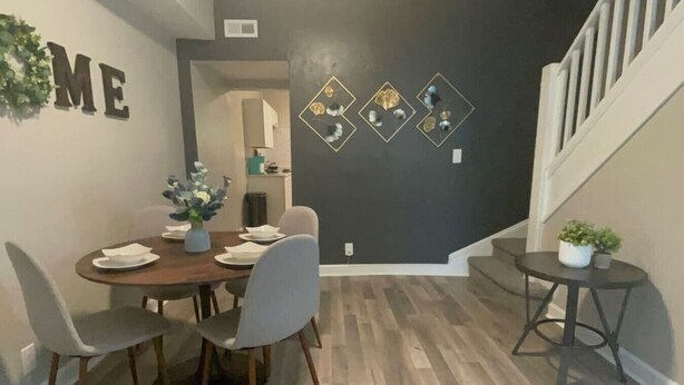 A dining area with a wooden table and chairs, a vase with flowers, and a wall with decorative elements.