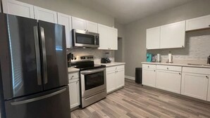 A modern kitchen with stainless steel appliances, white cabinetry, and a wooden floor.