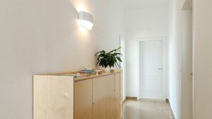 A hallway with a wooden cabinet, a potted plant, and a white door at the end. - Ammarèa B&B (Ugento)