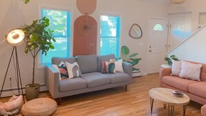 A living room with a grey sofa, a pink sofa, a round coffee table, and a floor lamp. - Tranquil Cape getaway 4BD 2BA with AC, Family and Pet Friendly!  (Mashpee)