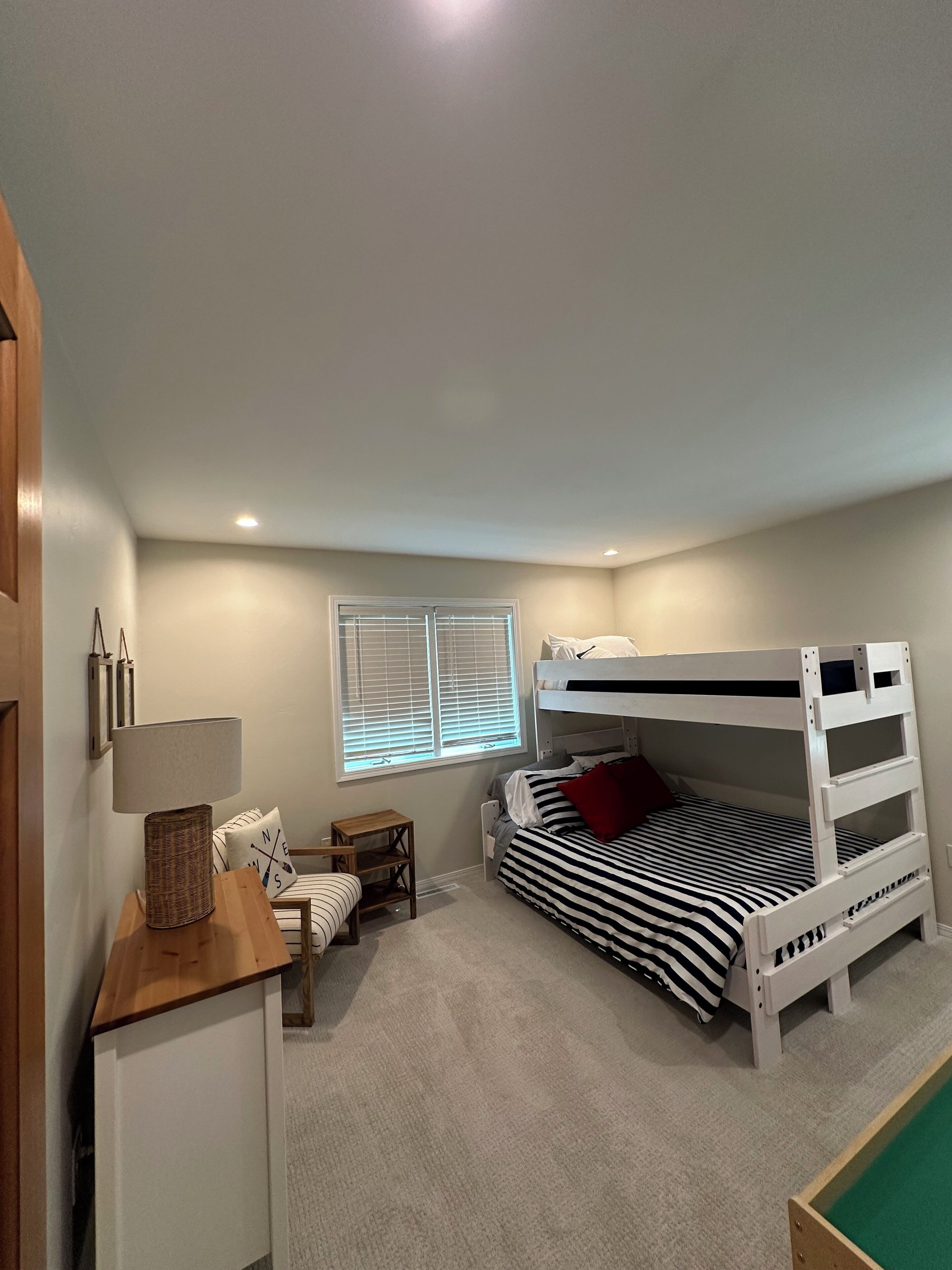 A bedroom with a bunk bed, a desk with a lamp, a small table, and a window with blinds.