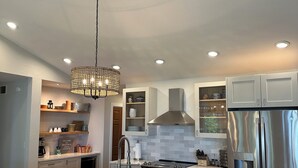 A modern kitchen with a large island, stainless steel appliances, and a hanging light fixture. - Enjoy nightly sunsets at this Beautiful Door County Waterfront Home (Sturgeon Bay)