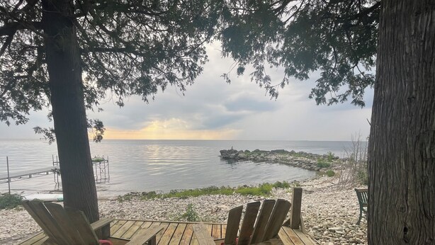 A wooden deck with two chairs facing a rocky shoreline and the sea. - Enjoy nightly sunsets at this Beautiful Door County Waterfront Home (Sturgeon Bay)