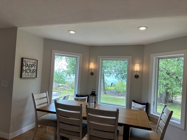 Un comedor con mesa y sillas, ventanas amplias con vistas al exterior y un cartel fijado en la pared.