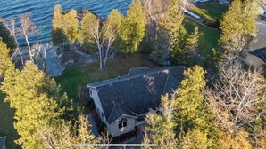 An aerial view of a house with a sloped roof, surrounded by trees and a body of water. - Enjoy nightly sunsets at this Beautiful Door County Waterfront Home (Sturgeon Bay)