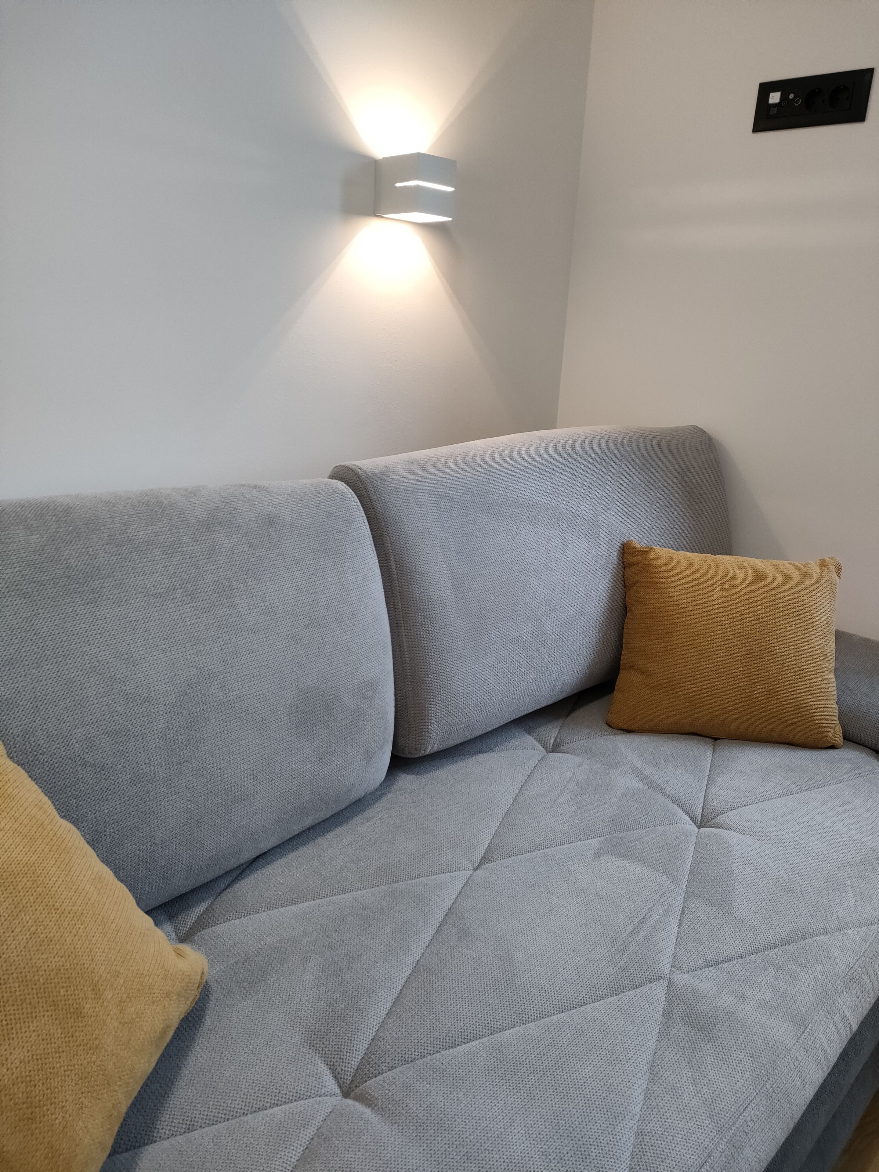 Un sofá gris con tela texturizada y un cojín de color mostaza.