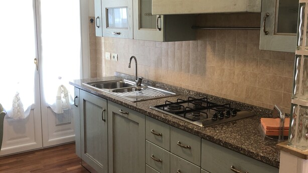 A kitchen with light green cabinets, a granite countertop, a stainless steel sink, and a gas stove. - Comfortable Apartment center Sarzana (Sarzana)