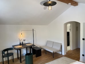 Un'area pranzo moderna con tavolo, sedie e lampada a sospensione. Nella stanza c'è anche un divano e un cestino.