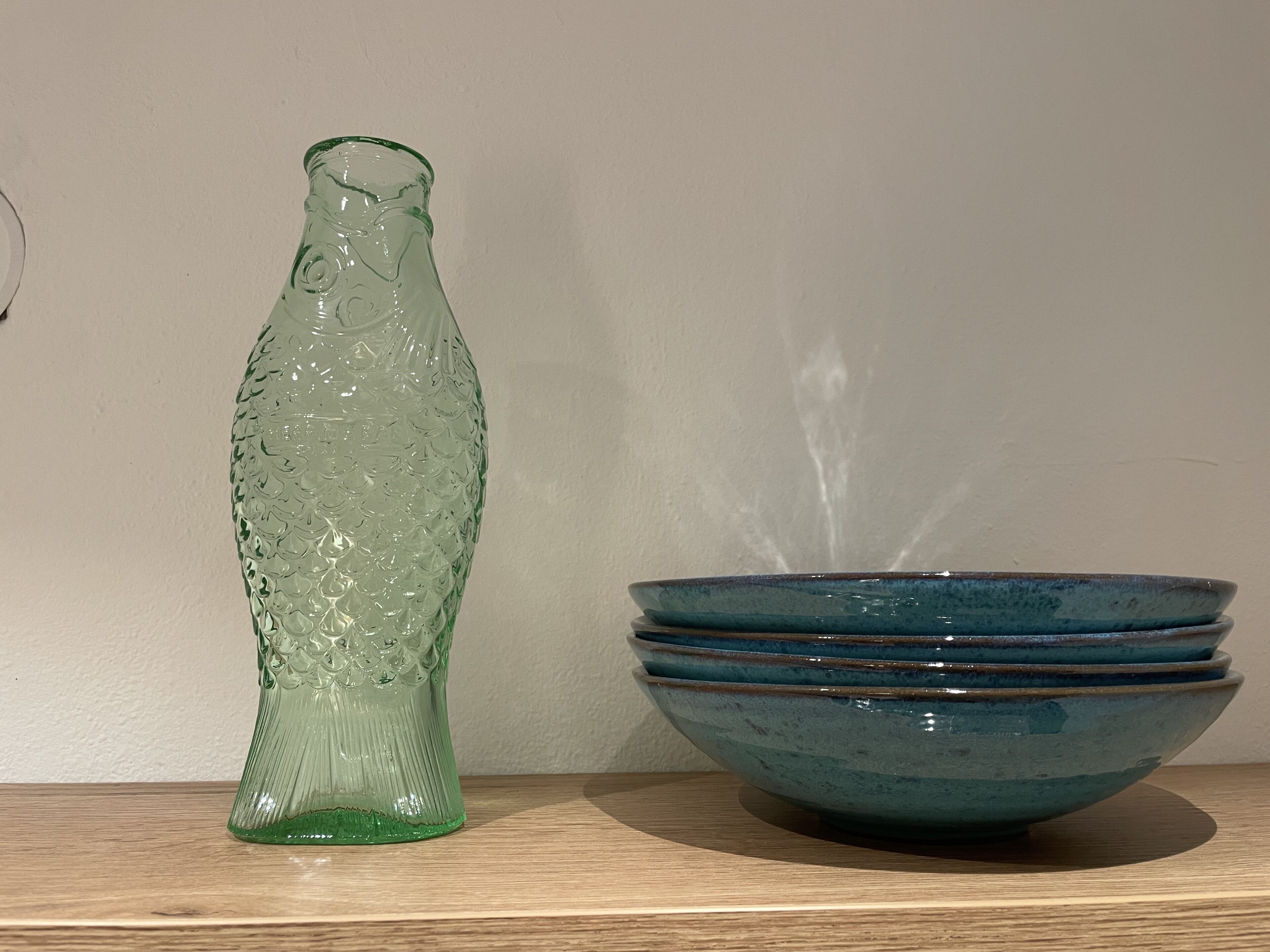 A green glass bottle and a stack of blue ceramic bowls on a wooden shelf.