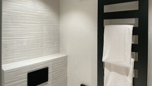 Un baño con pared blanca con textura, un perchero negro y un respiradero negro.