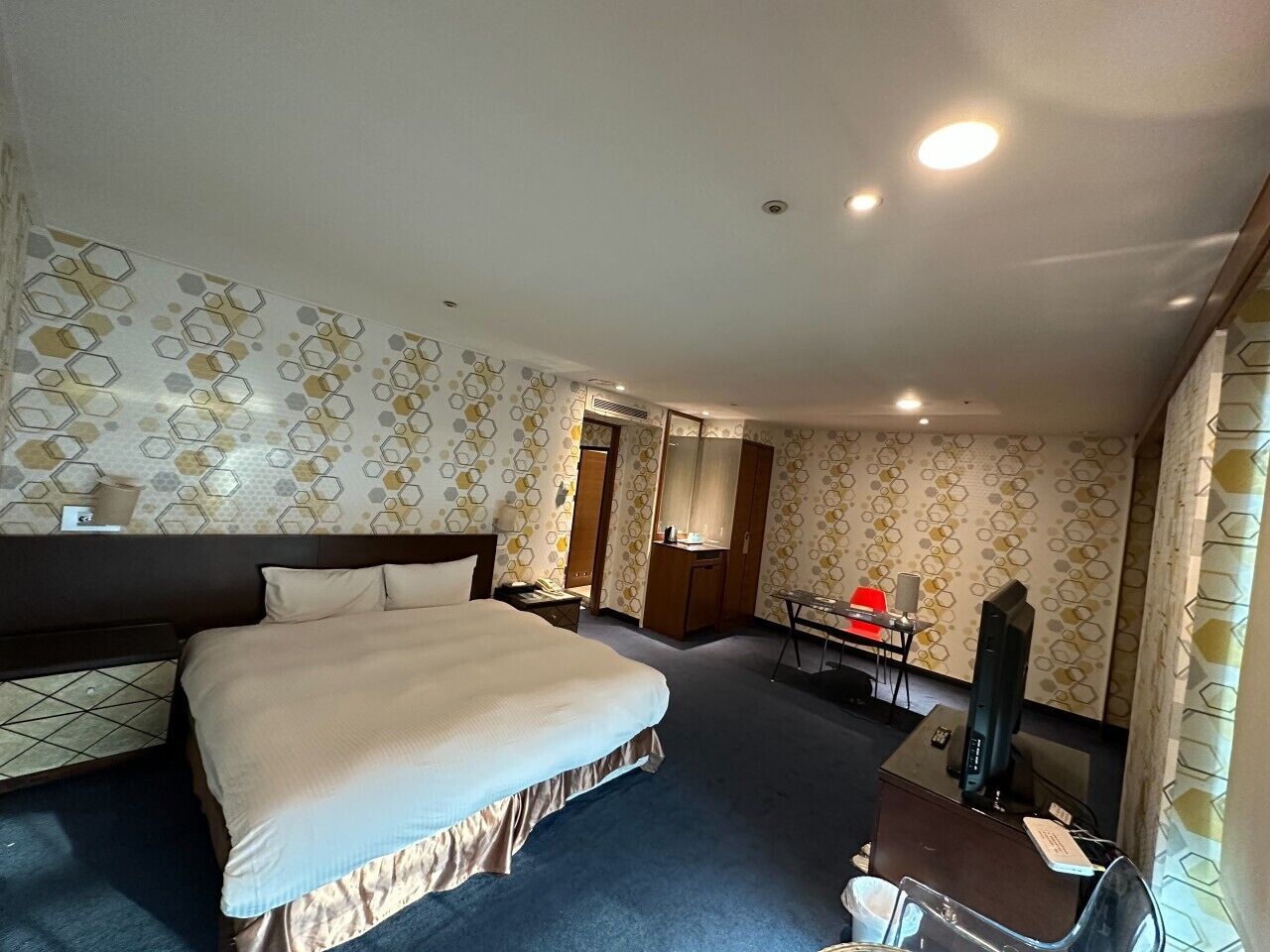 A hotel room with a large bed, a desk, a mirror, and a TV.