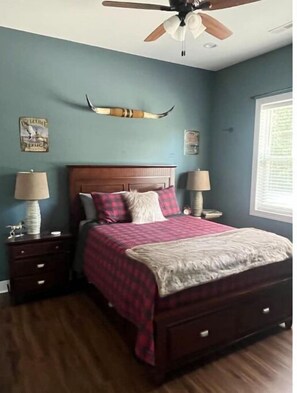A bedroom with a wooden bed, two nightstands, a ceiling fan, and a window with blinds.