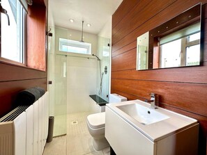 A modern bathroom with a glass shower enclosure, a white toilet, and a sink with a wooden panel wall. - Stunning Panoramic Sea View Beach Location 2 bed (bournemouth)