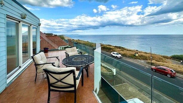 A balcony with a table and chairs overlooking a coastal road and ocean. - Incredible Panoramic Sea View 2 Bedroom Sleeps 4 WOW! (bournemouth)