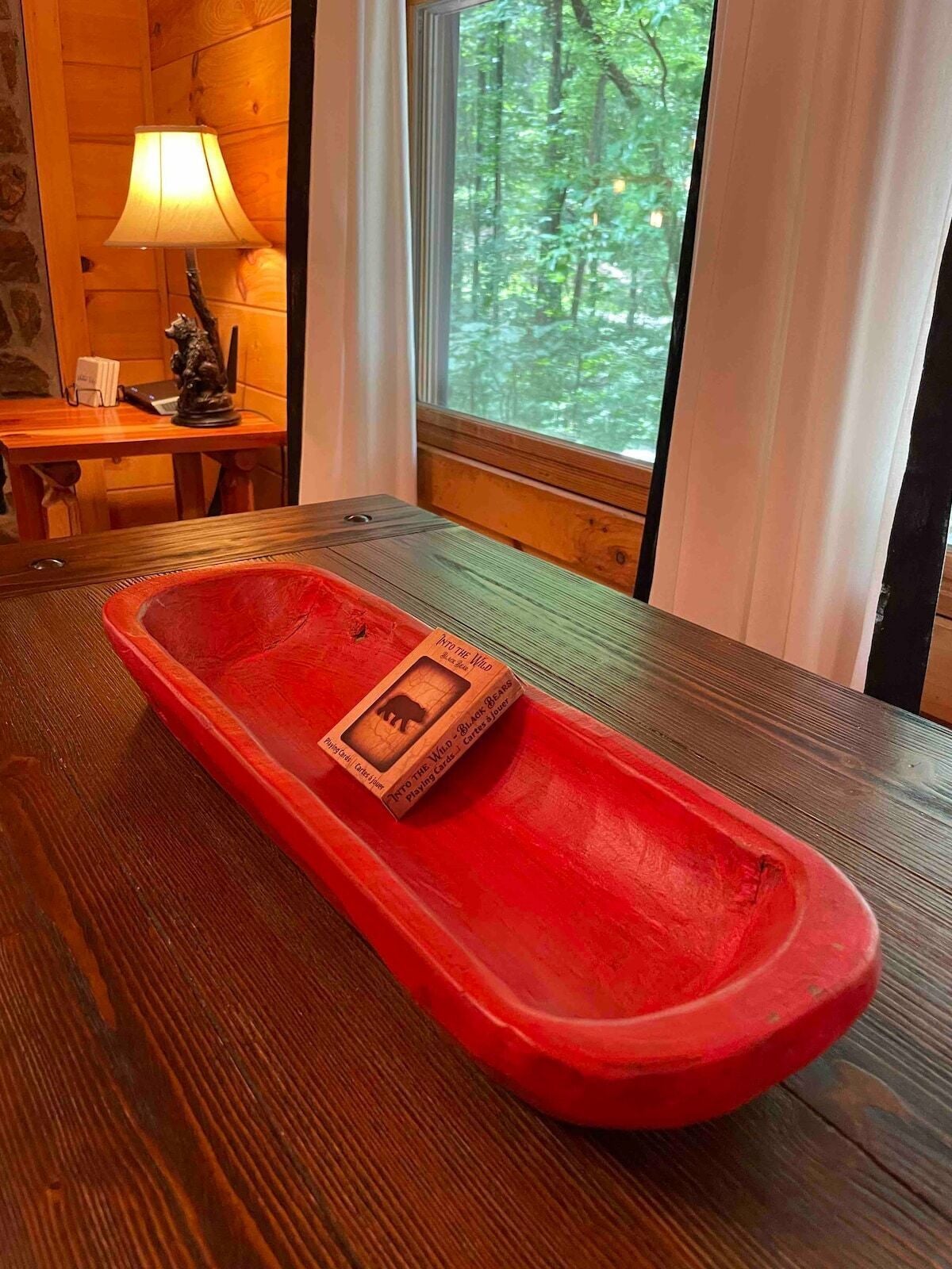 A wooden table with a red tray, a lamp, and a window with a forest view.
