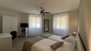 Quarto de hotel com duas camas, uma escrivaninha, uma cadeira, uma televisão e um ventilador de teto.