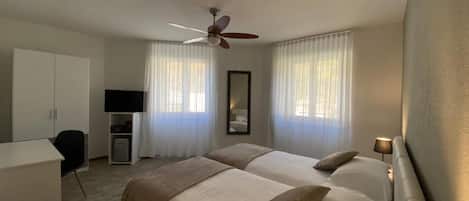 Una habitación de hotel con dos camas, un escritorio, una silla, un televisor y un ventilador de techo.