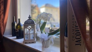 Um parapeito de janela com um pequeno candeeiro em formato de casa, uma orquídea em vaso e uma garrafa de champanhe.