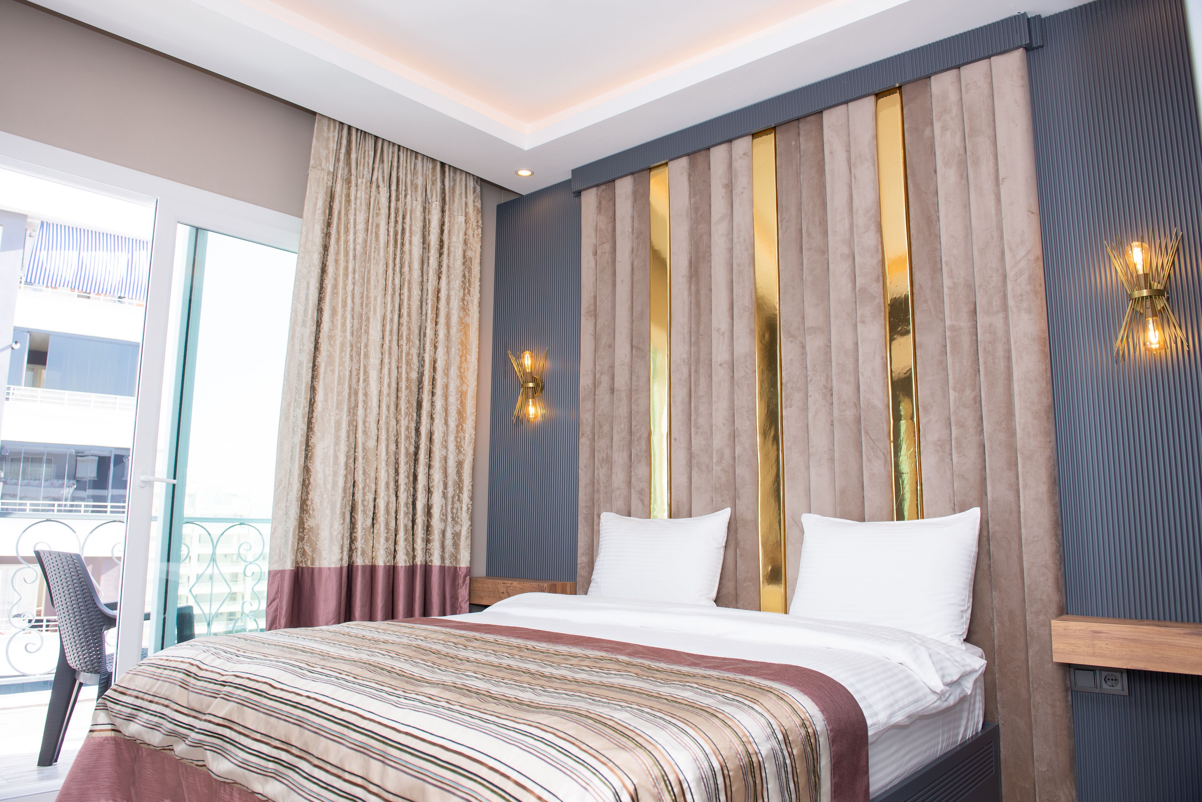 A hotel room with a large bed, a view of the balcony, and a modern light fixture.