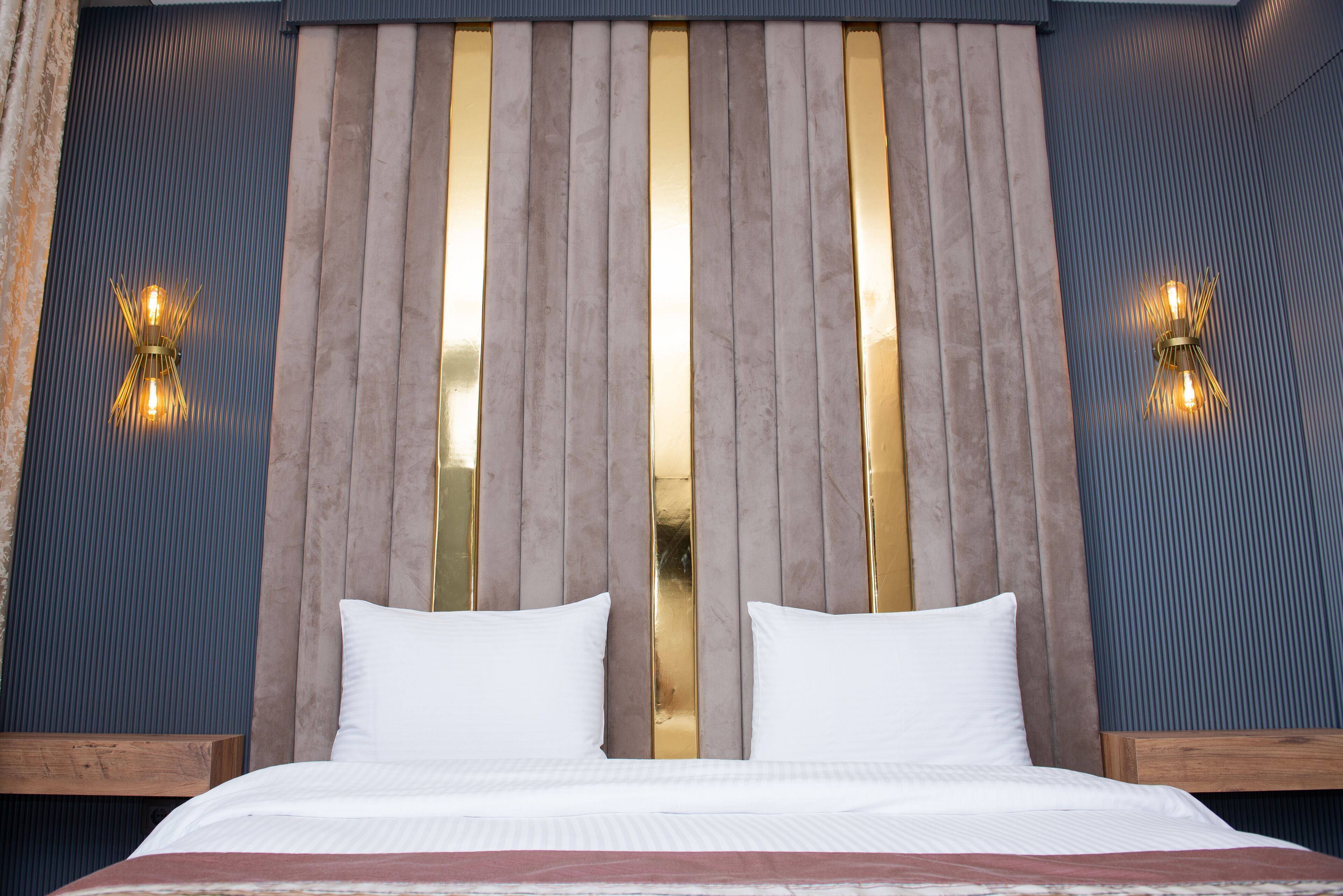 A hotel room with a large bed, two bedside tables, a wooden headboard, and wall-mounted lighting.