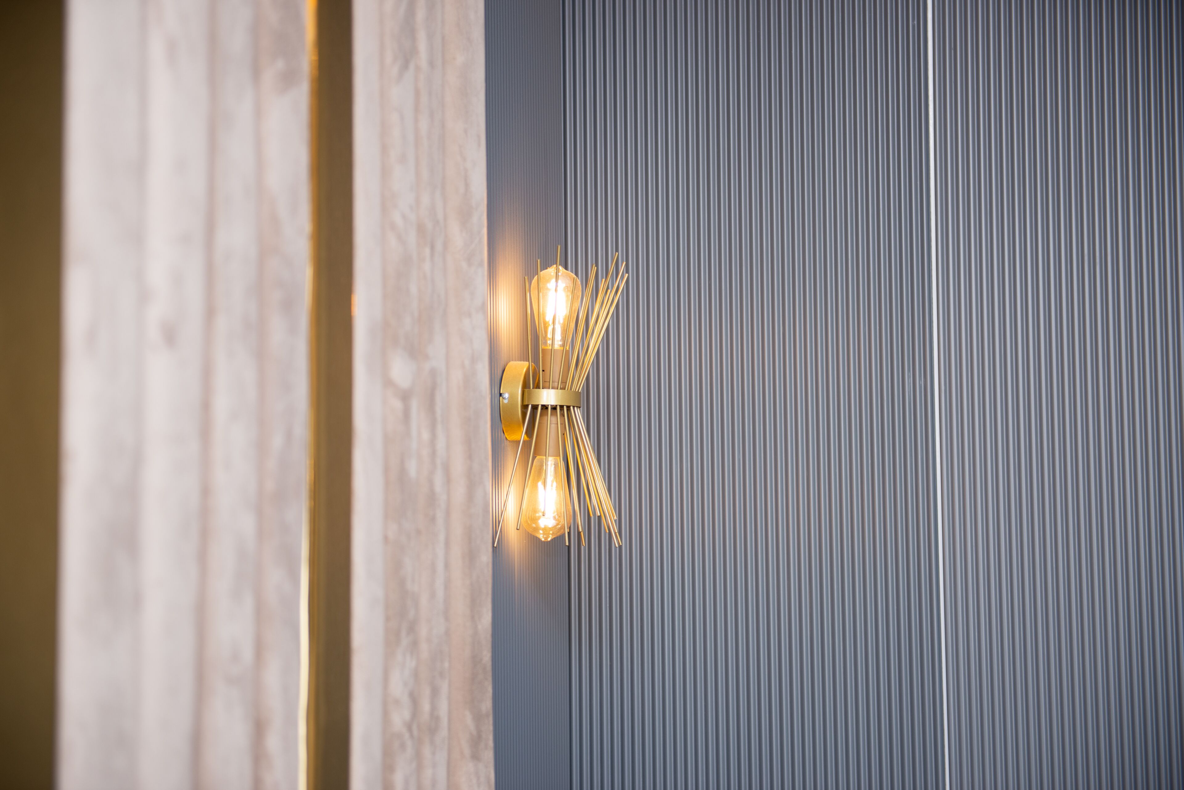 A wall-mounted light fixture with a unique design, possibly a modern or industrial style, against a textured wall.