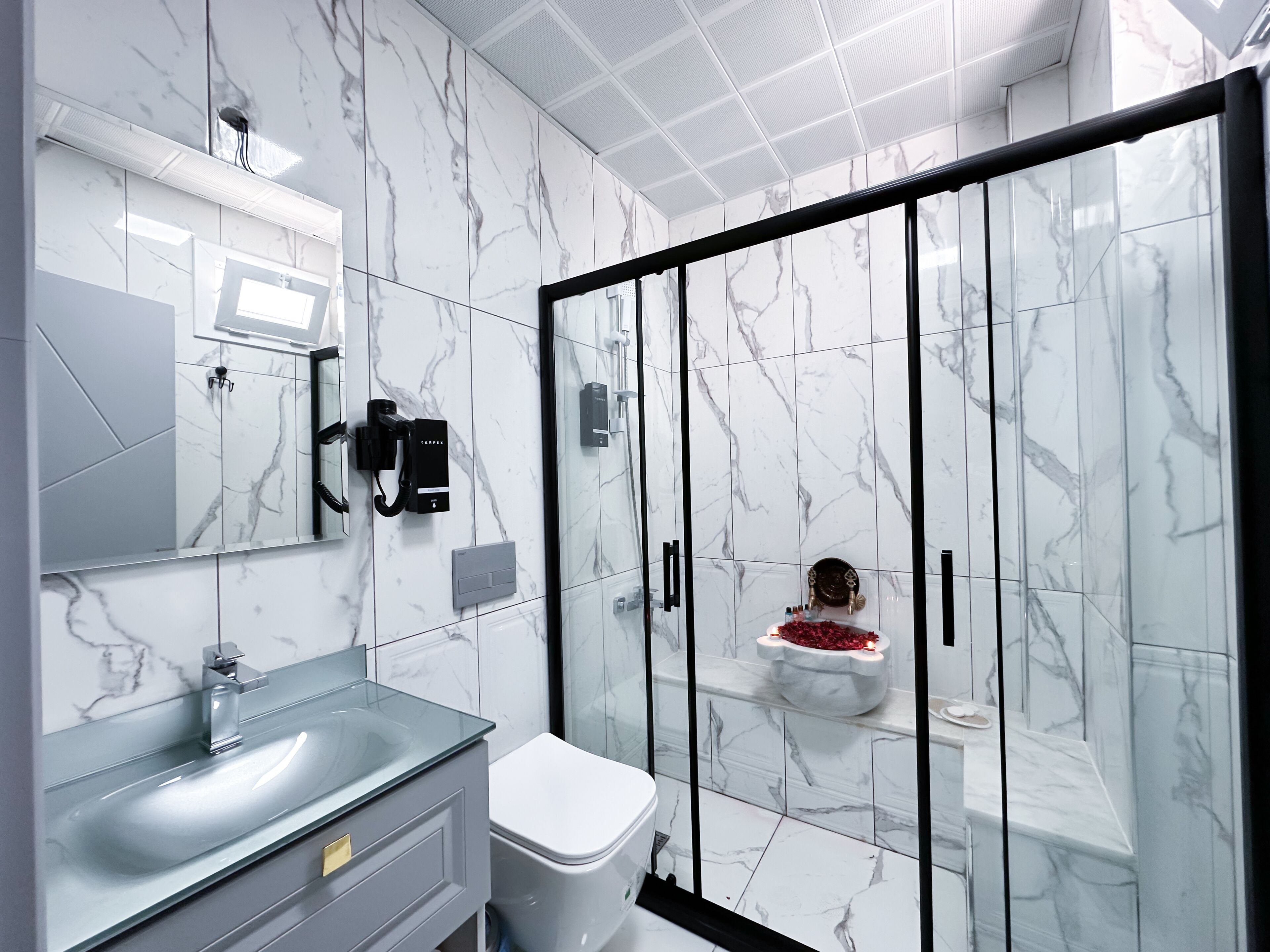 A modern bathroom with a glass-enclosed shower, marble walls, a glass sink, and a toilet.