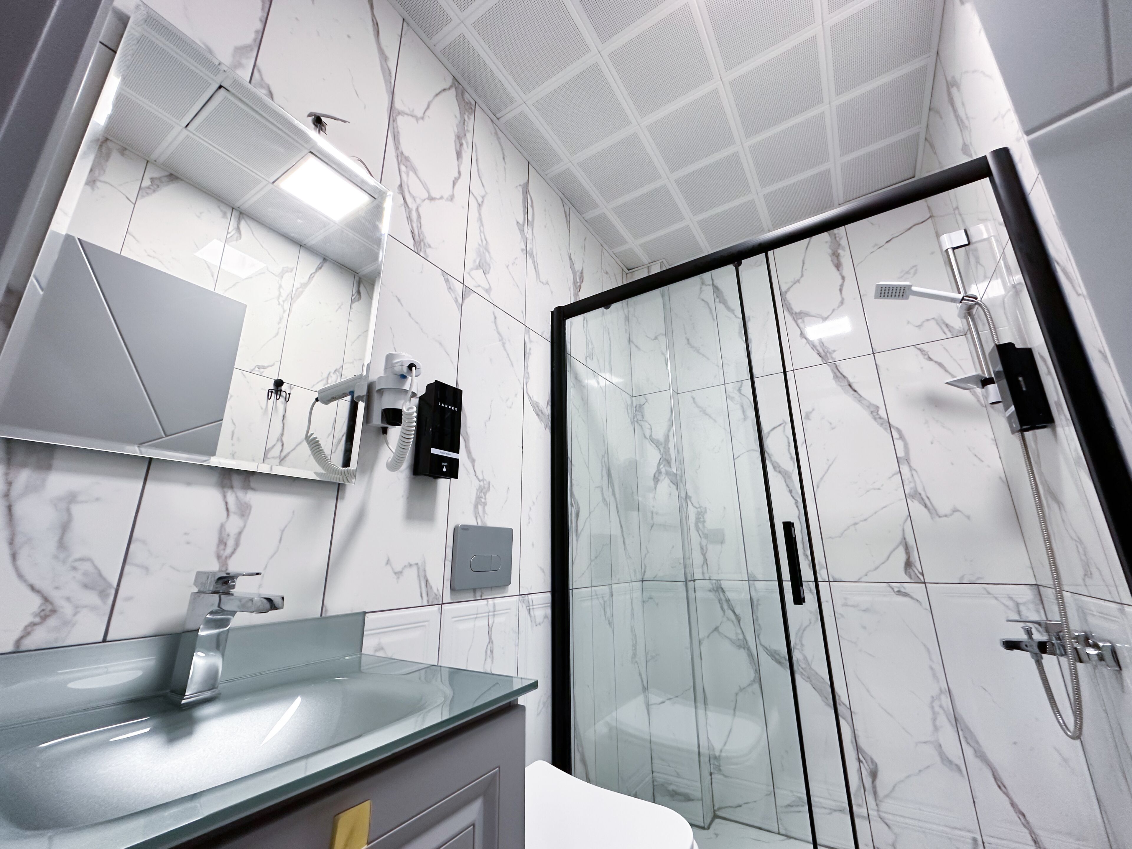 A modern bathroom with a glass shower enclosure, a glass sink, and a marble-tiled wall.