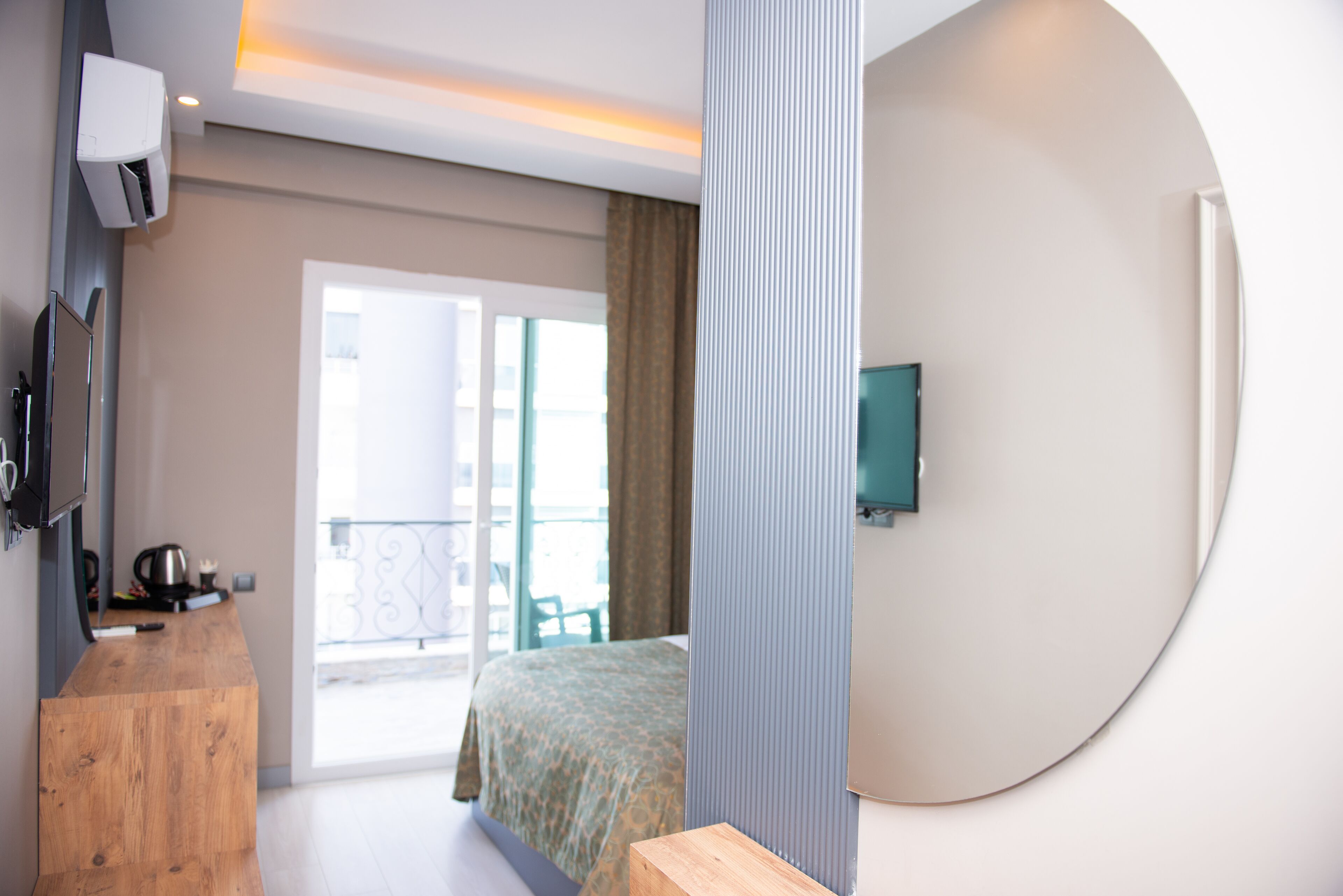 Ein modernes Hotelzimmer mit Schreibtisch aus Holz, einem Bett mit gemustertem Überwurf, einem an der Wand montierten Fernseher und einem Balkon mit Aussicht.