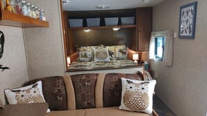 A cozy room with a sofa, a bed with a quilt, and a shelf with jars.