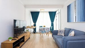 Una sala de estar moderna con un televisor de pantalla plana, mueble de entretenimiento de madera, sofá azul y un comedor con mesa y sillas.