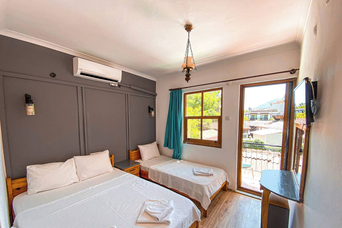 A room with two beds, a ceiling fan, an air conditioning unit, a window with curtains, and a view of the outside.