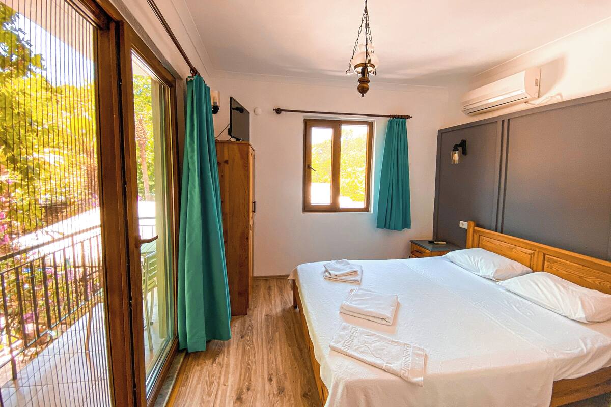 A bedroom with a bed, a window, an air conditioning unit, and a view of greenery outside.