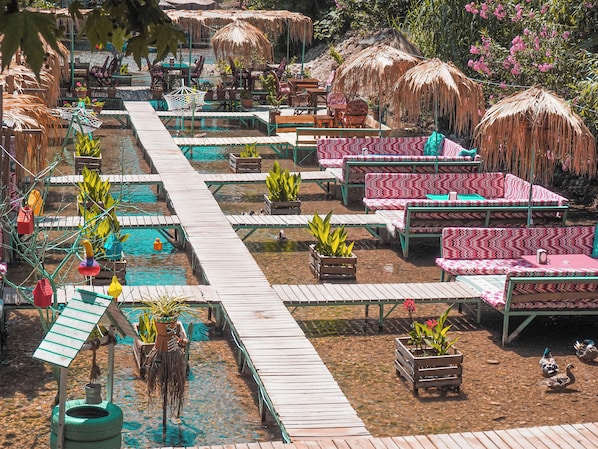 A pool area with wooden deck, lounge chairs, and thatched umbrellas. - Adrasan River Hotel (Kumluca)