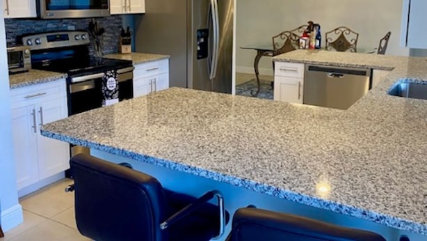 A modern kitchen with white cabinets, stainless steel appliances, granite countertops, and two black bar stools.