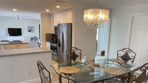 A modern kitchen with a large island, stainless steel appliances, and a dining area with a glass table and ornate chairs.