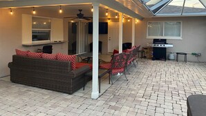 A covered patio area with a ceiling fan, outdoor seating, and a grill.