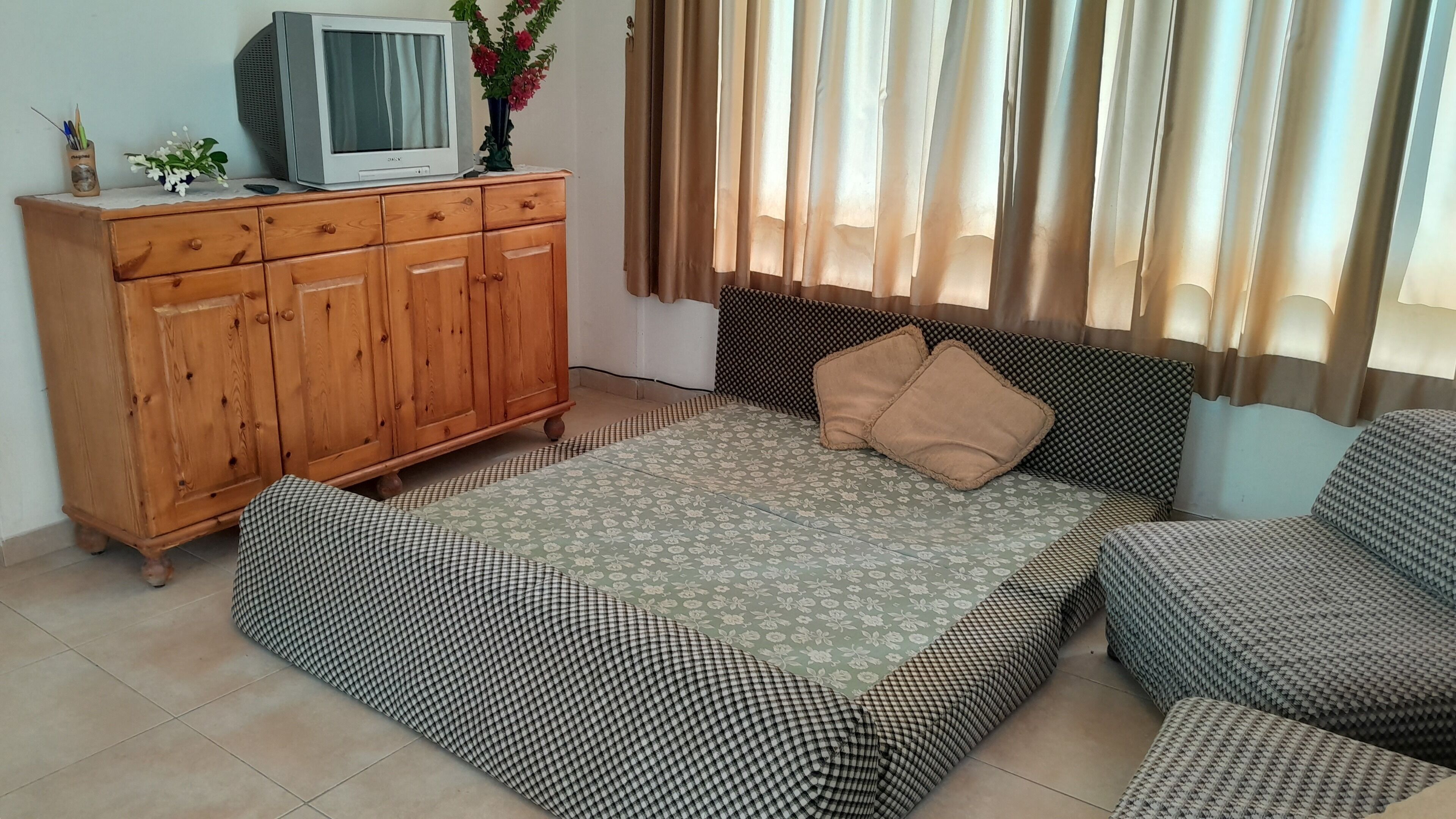 A bedroom with a bed, a wooden wardrobe, a television, and a window with curtains.