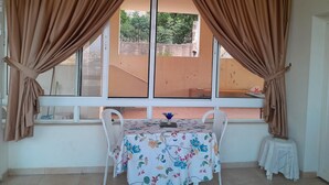 A room with a window, a table with a floral tablecloth, and curtains. - Authentic Lebanon - Charming, welcoming property in the heart of Magdouché (Maghdoucheh)