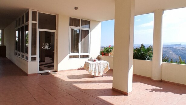 A spacious room with large windows, a tiled floor, and a table with a tablecloth. - Authentic Lebanon - Charming, welcoming property in the heart of Magdouché (Maghdoucheh)