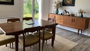 Ruokailutila, jossa on puinen pöytä ja tuolit, koriste-esineitä sisältävä kaappi sekä näkymä lasiovesta.