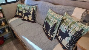 Um sofá com almofadas estampadas, uma janela e uma estante com potes.