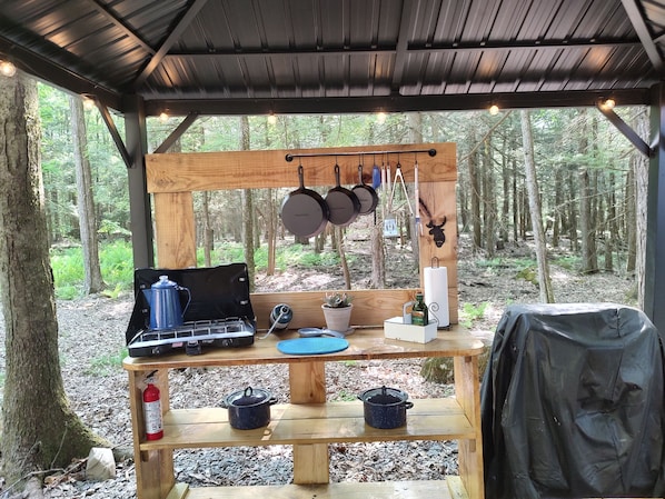 Cucina esterna rustica con fornello a gas, pentole e utensili appesi.