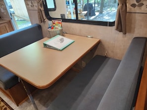 Interni di un camper compatto con tavolo da pranzo, una panca imbottita e una finestra con vista sull'esterno.
