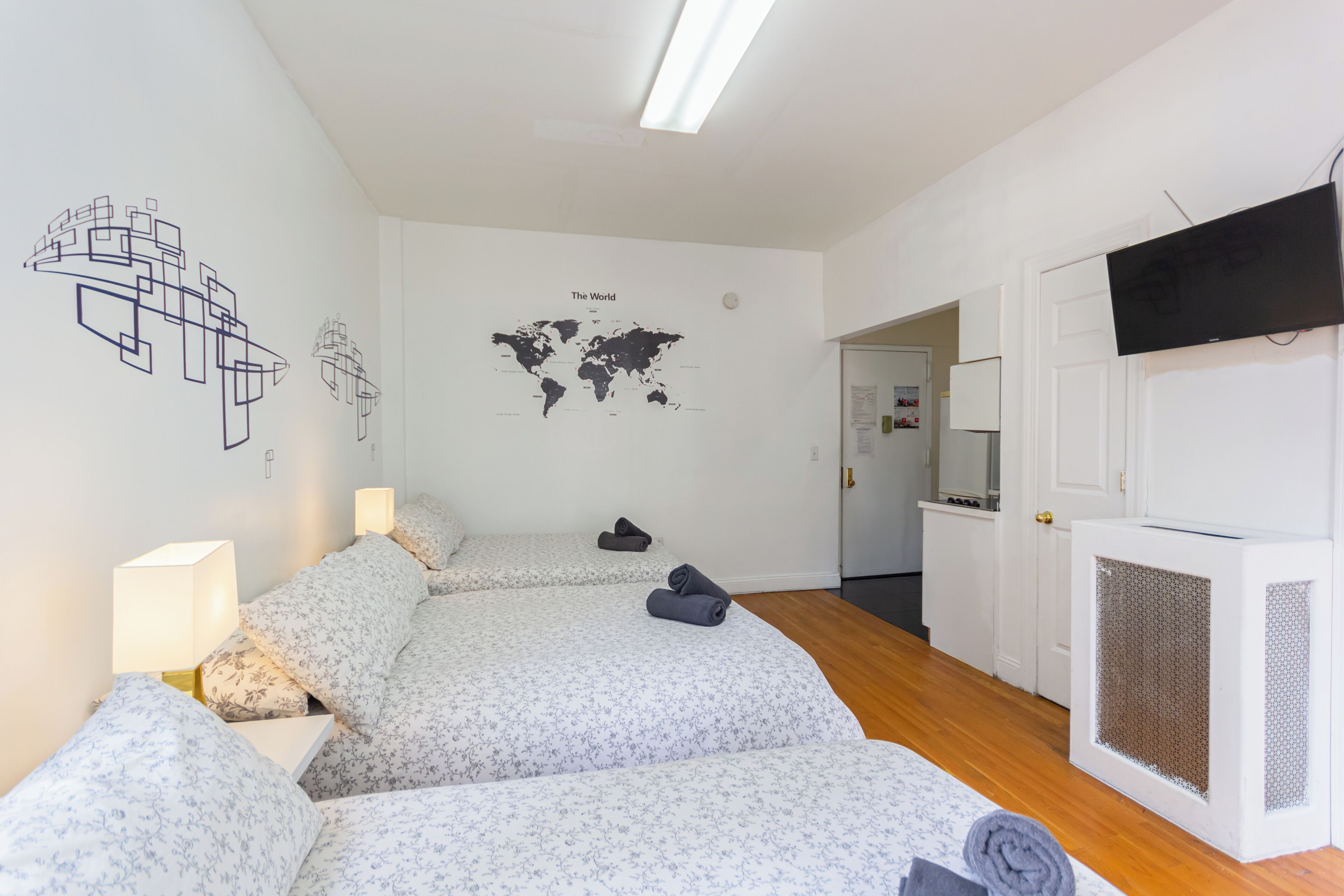 A hotel room with two beds, a world map on the wall, a TV, and a white door.